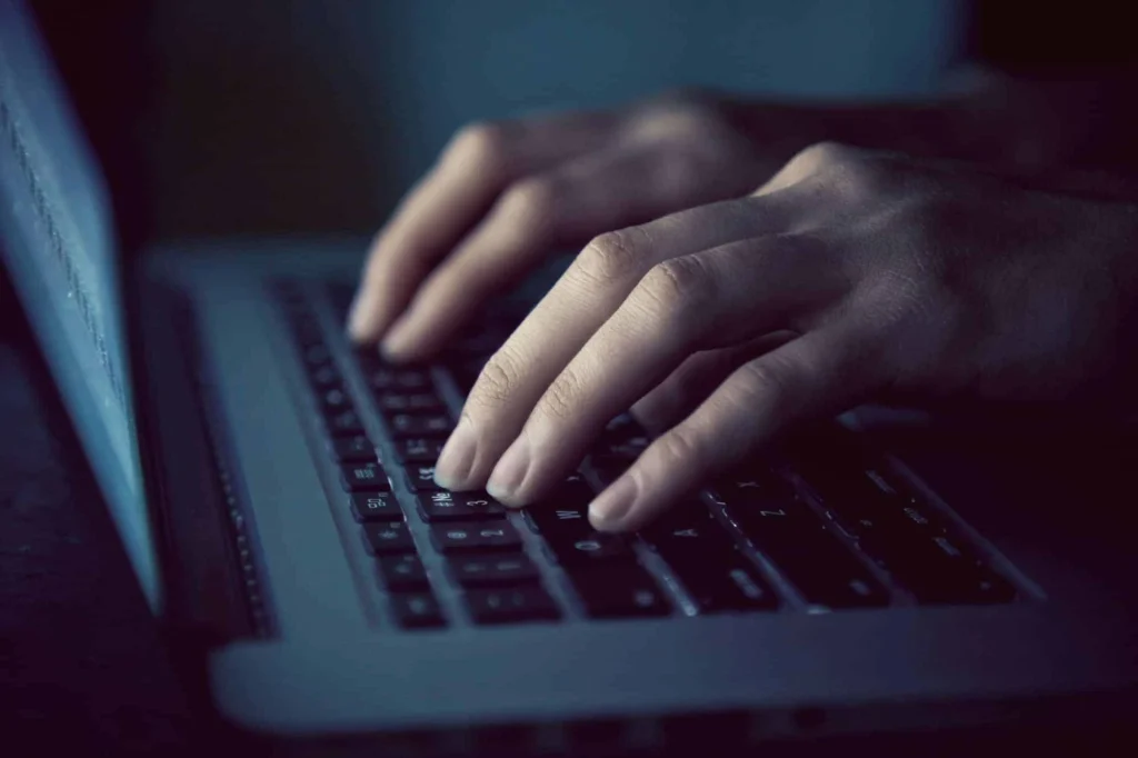 IT guy typing on laptop keyboard in the dark
