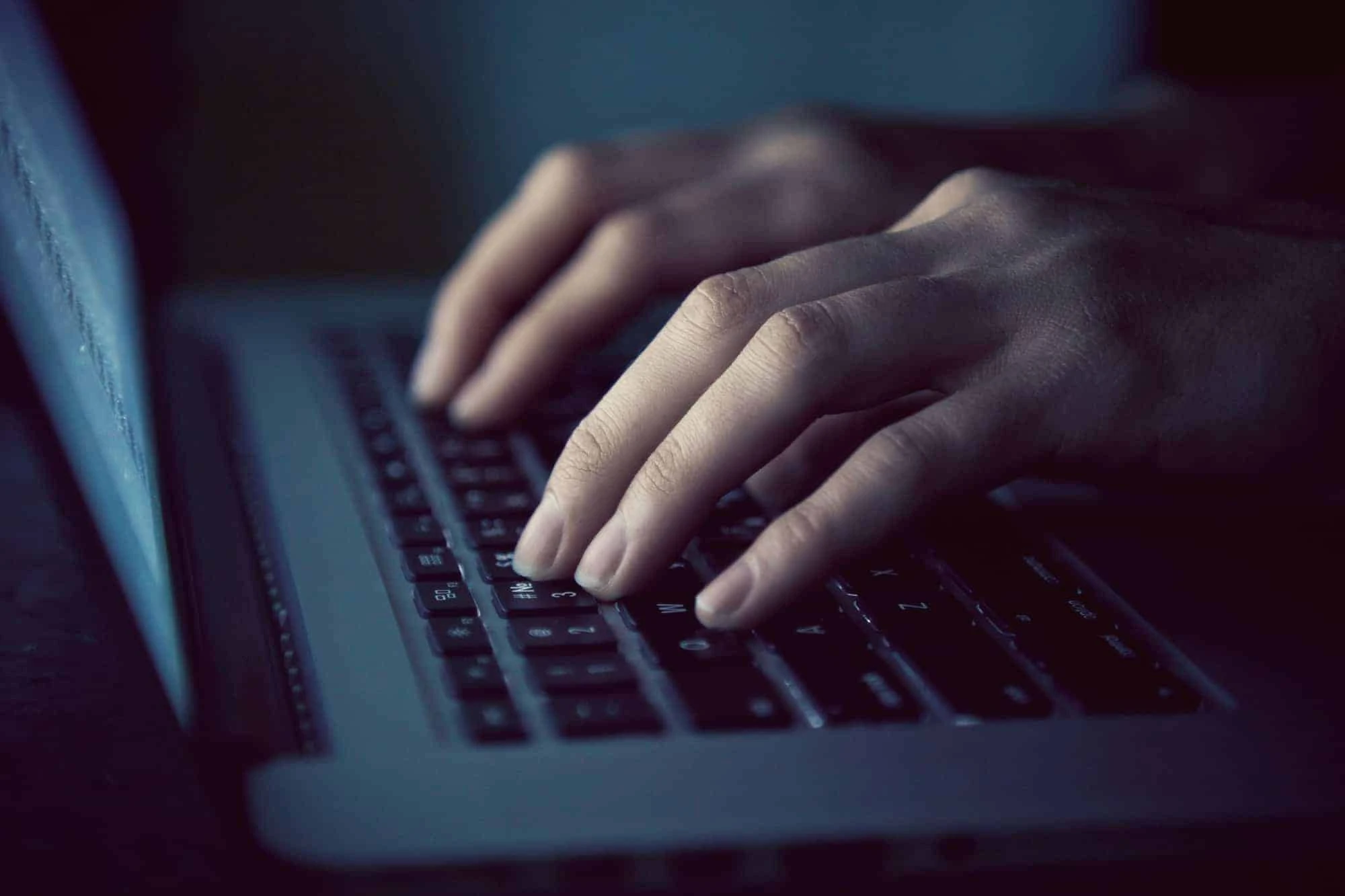 IT guy typing on laptop keyboard in the dark
